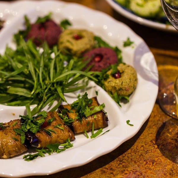 Georgian appetizers: eggplant rolls with herbs, and colorful dips on a white plate.