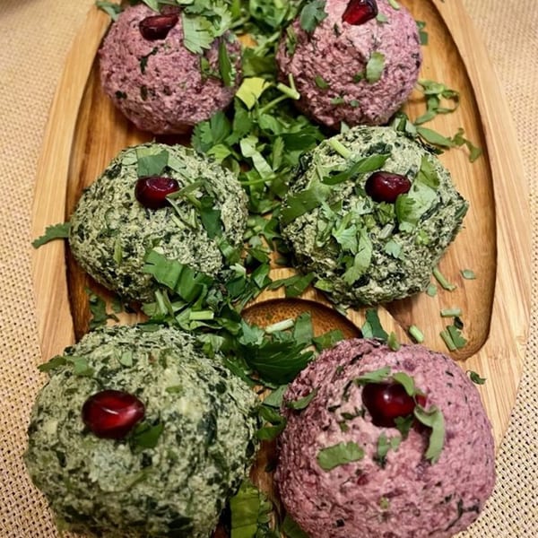 Six vibrant Georgian Pkhali balls, green and purple, garnished with fresh herbs and pomegranate seeds.