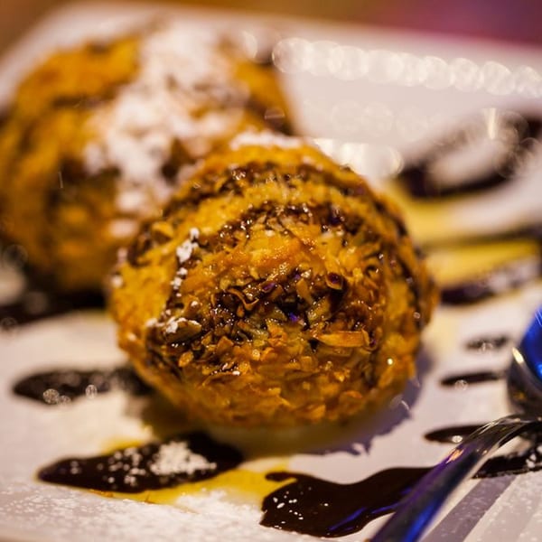 Two fried ice cream balls with chocolate drizzle and powdered sugar on a white plate.