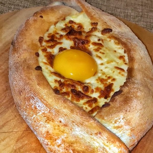 A Georgian khachapuri, a boat-shaped bread filled with melted cheese and topped with a raw egg yolk.